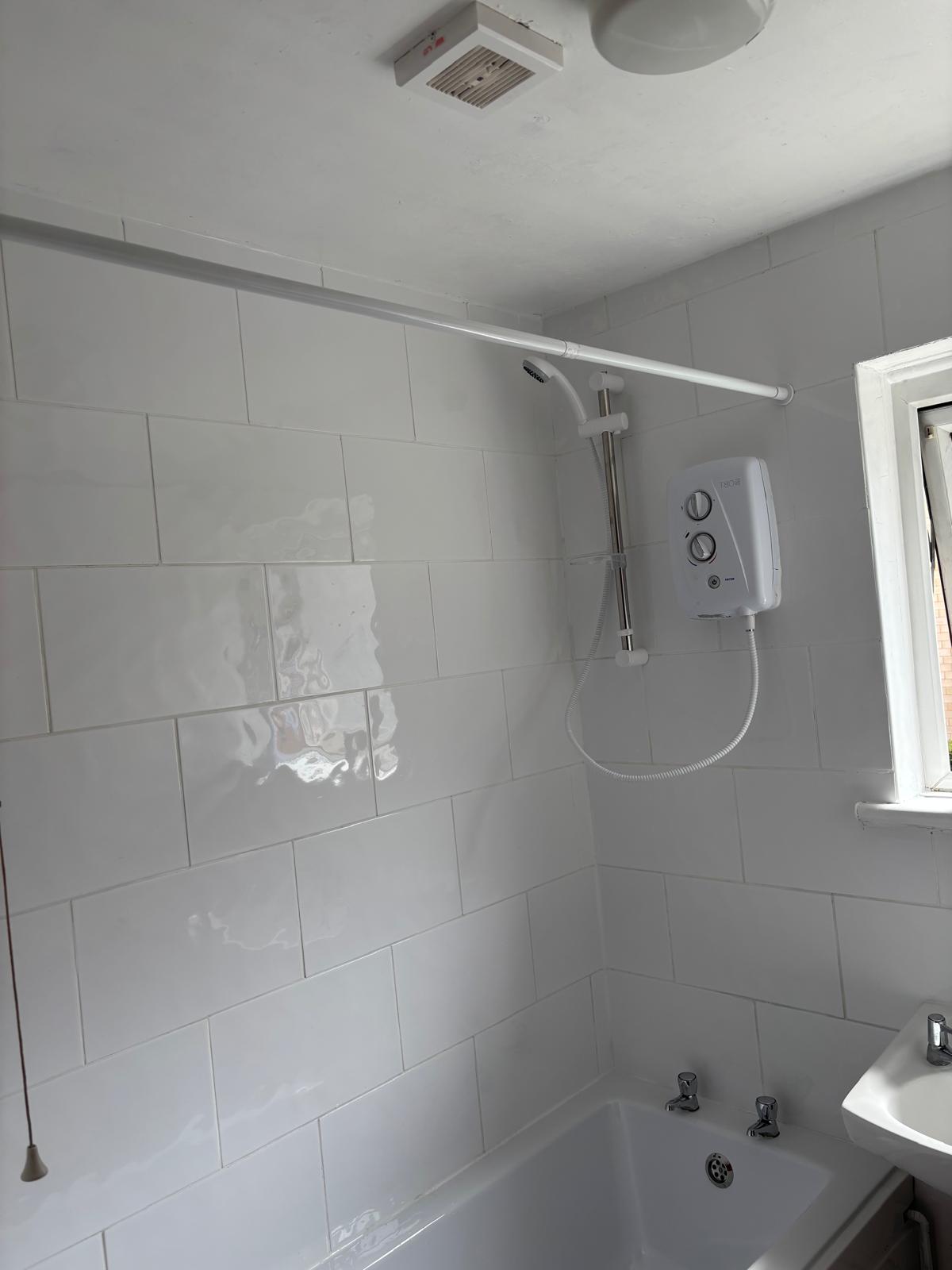 Tiled bathroom wall with an electric shower fitted over the bath